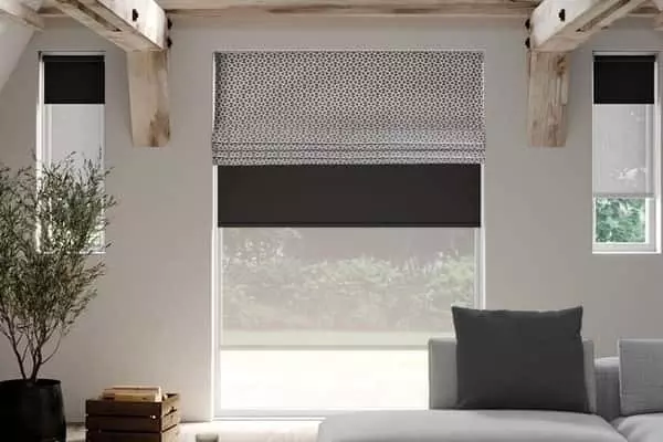 Kétféle római roló egy ablakon – stílus és funkció tökéletes egyensúlya Egymás elé szerelt mintás és egyszínű római rolók modern, gerendás nappaliban